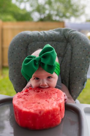 A playful watermelon slice decorated with a green bow sits on a chair in an outdoor setting.