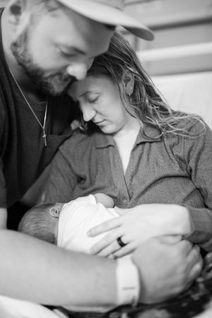 Black and white intimate photograph of parents gazing lovingly at their newborn baby in a tender hospital moment.