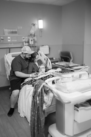 Black and white photo showing tender hospital room moment between patient and visitor near a window.