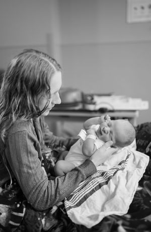 Black and white sequence of images showing someone holding and cradling a baby wrapped in white blankets in a tender moment.