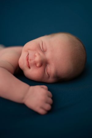 Peaceful sleeping newborn baby with tiny fists curled on deep blue background.