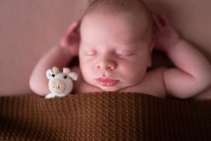 Newborn baby peacefully sleeping on soft brown textured blanket in gentle studio lighting.