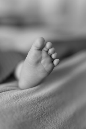 Close-up black and white photo of a tiny baby foot showing delicate toes.