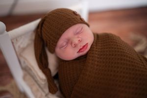Close up photo of a newborn baby sleeping peacefully on soft brown knitted fabric.