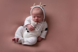 Sleeping newborn in white outfit and bunny ear bonnet arranged in artistic photography setting.