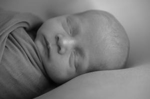 Close-up black and white portrait of a sleeping baby showing peaceful expression against light background.