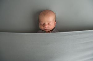 A sleeping newborn baby peacefully rests against soft gray bedding.