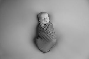 Peaceful sleeping newborn swaddled in grey wrap during professional black and white studio photography session.