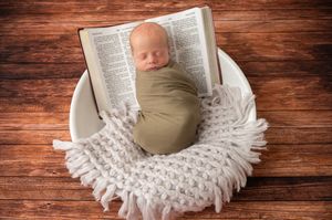 Sleeping newborn on soft white blanket with holy bible open beside them.