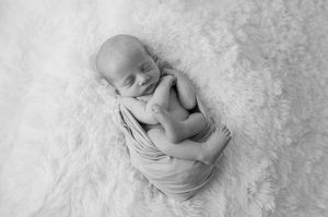 Side view of sleeping newborn in rust colored swaddle on textured white blanket.