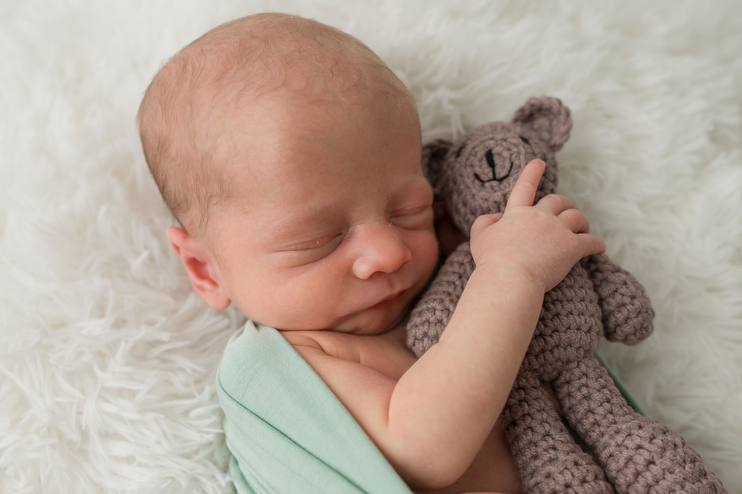 Five newborn portraits on white fabric showing baby with knit teddy bear in mint and neutral colors.