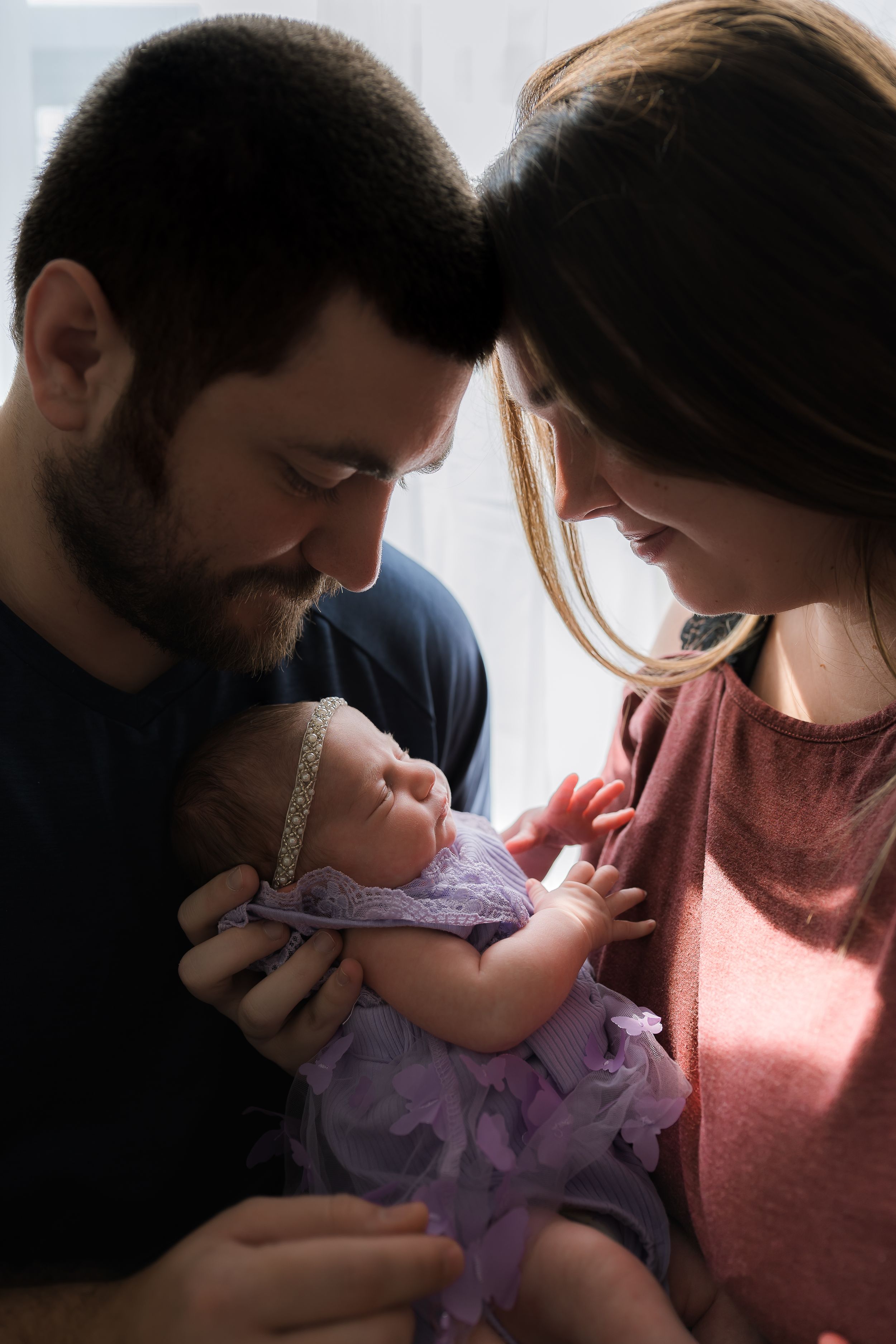 Loving parents hold and kiss their baby in a purple dress in a sequence of tender family moments.