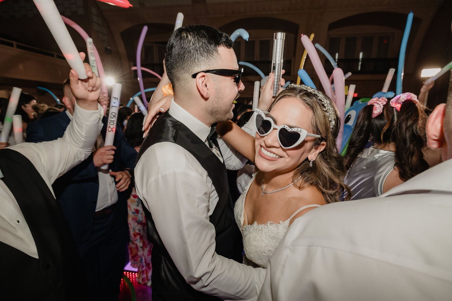 People dancing in a dimly lit venue with a festive party atmosphere and colored light sticks for Sacramento wedding reception