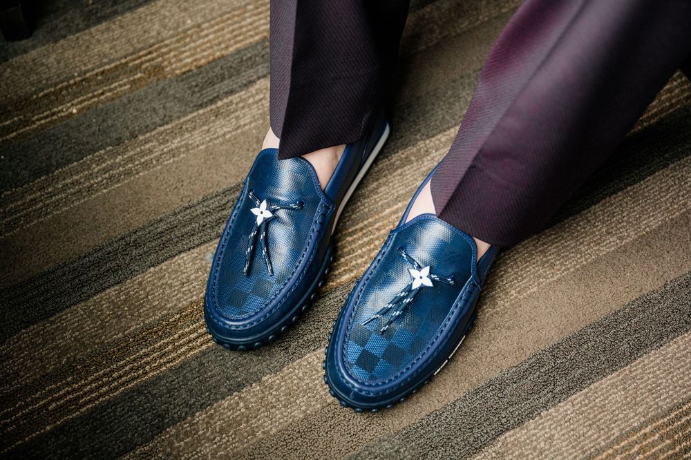 A pair of navy blue leather loafers with tassels on a wooden floor.