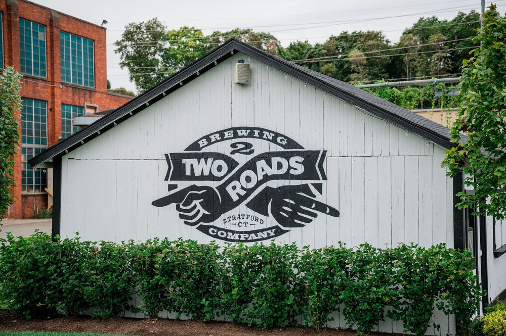 Two Roads Brewing Company exterior sign painted on white building wall with crossed baseball bats logo.