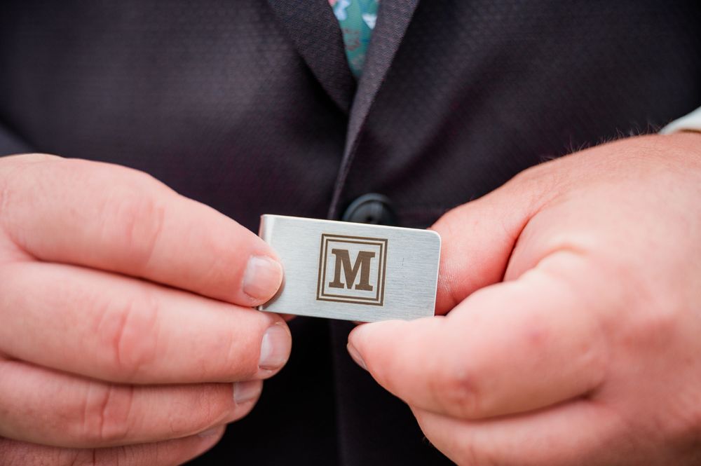 Close-up of hands holding a silver monogram cufflink with the letter M.