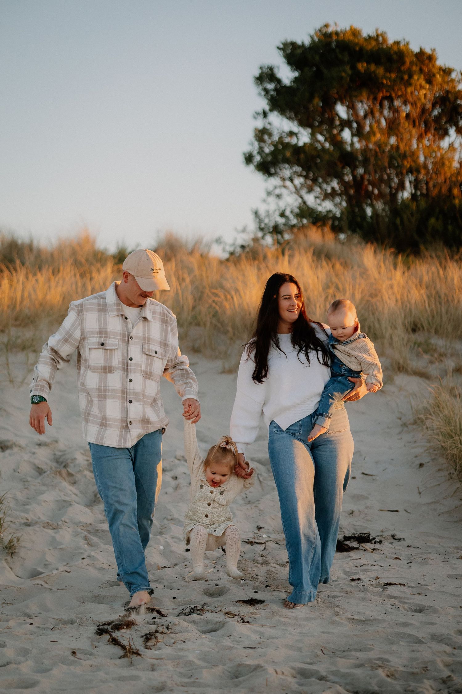 A tender beach moment at sunset with a toddler and adult sitting together on golden sand by the ocean.