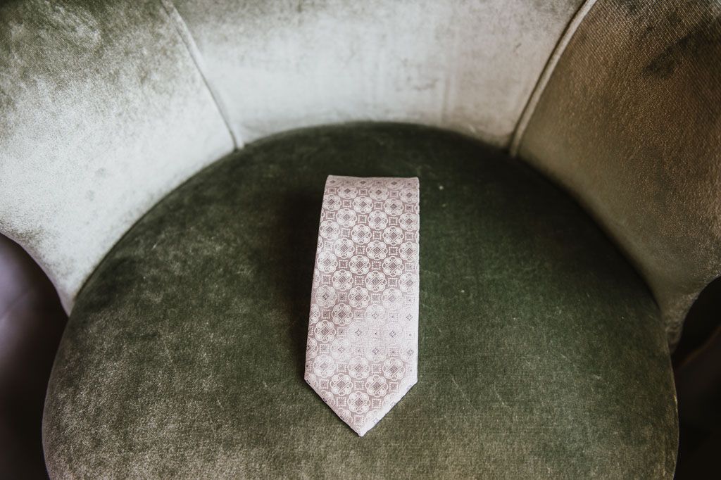 A pink patterned tie rests on a dark green velvet chair cushion.