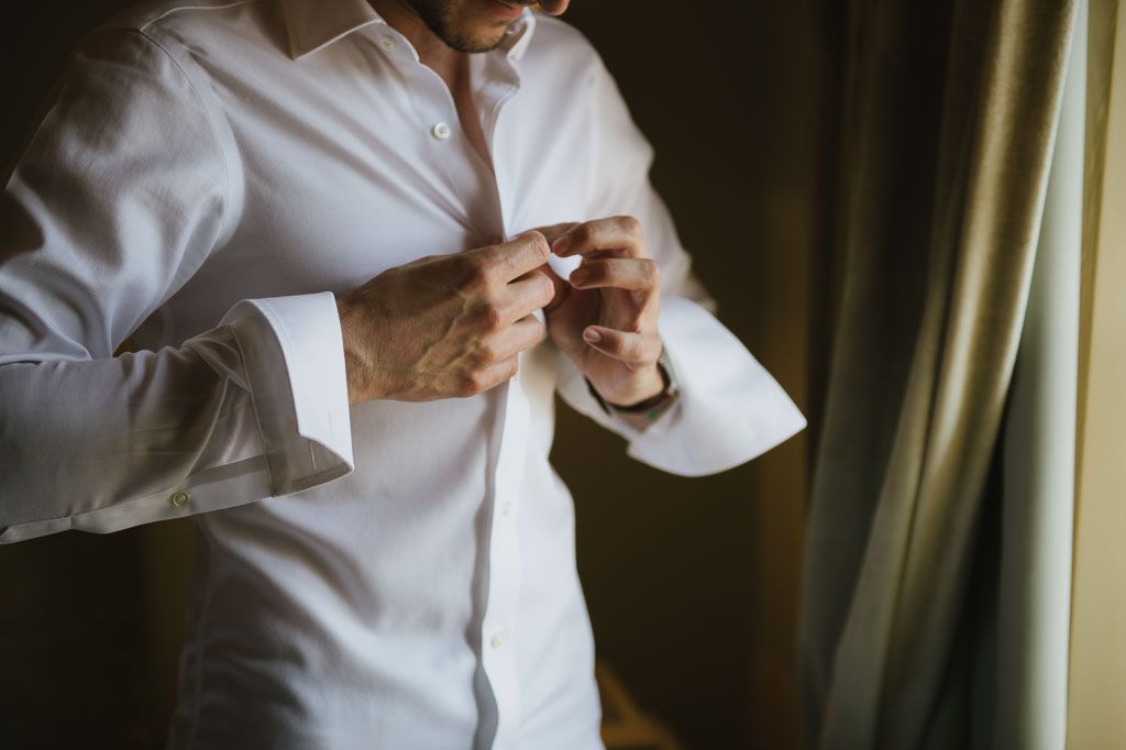 Close-up view of person in white dress shirt buttoning cuff during formal attire preparation.