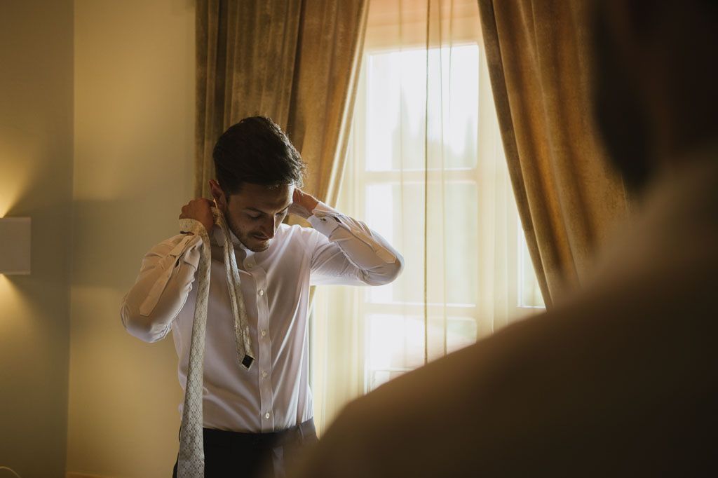 A person in a white shirt stands near a window with warm sunlight streaming through sheer curtains.