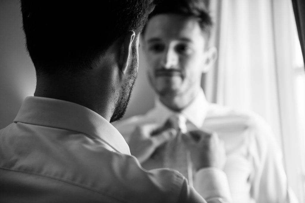 Black and white image of someone adjusting their bowtie while looking in a mirror.