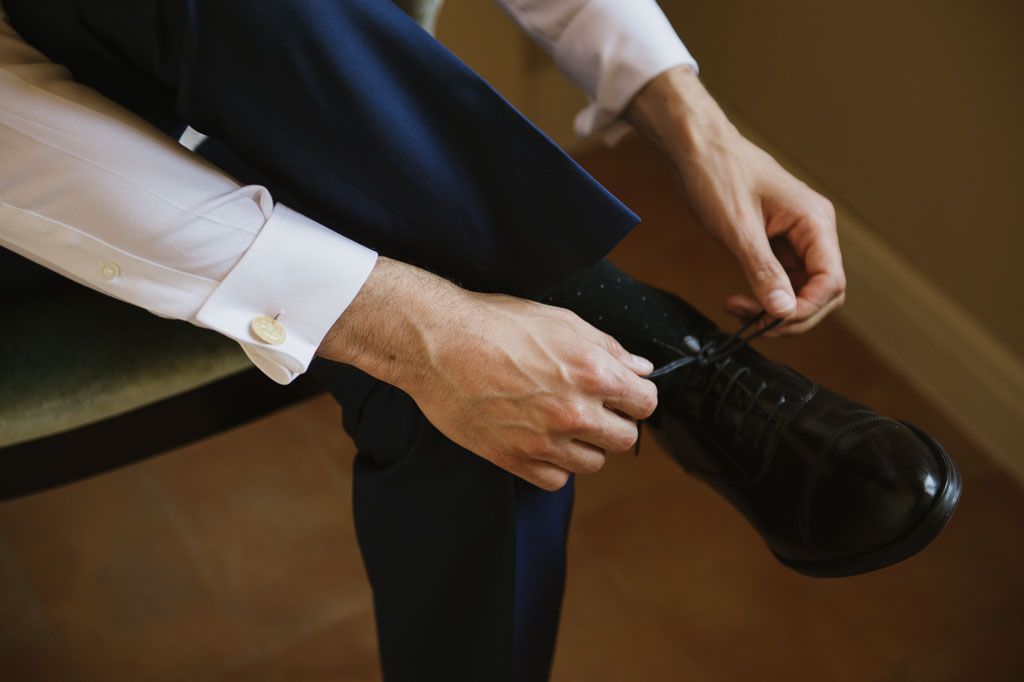 Close-up shot of hands adjusting cufflinks against a blurred brown background.
