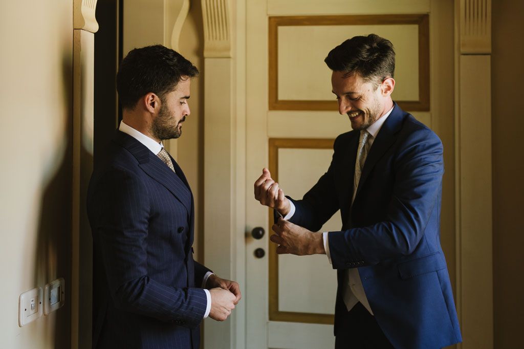 Two men in formal attire interact energetically while standing indoors.