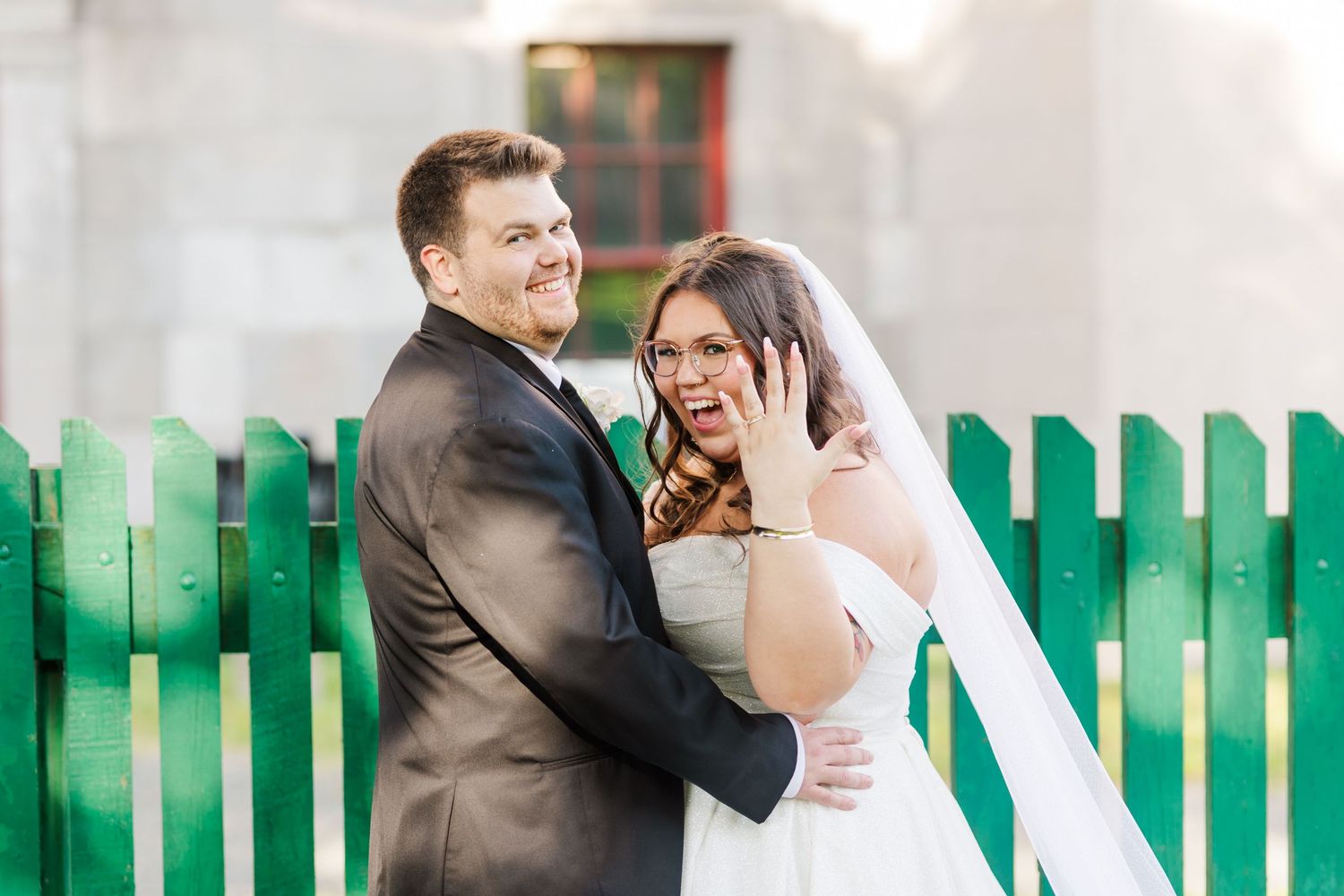A happy couple shares a laugh together in front of a bright green fence during their outdoor photo session.