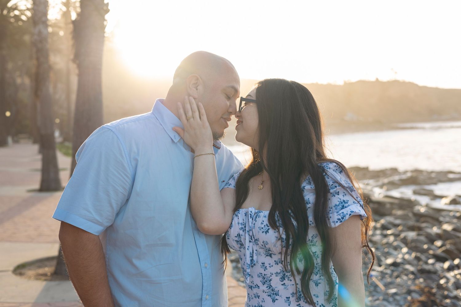 A couple shares a romantic moment during sunset at a beach while wearing coordinated blue outfits.