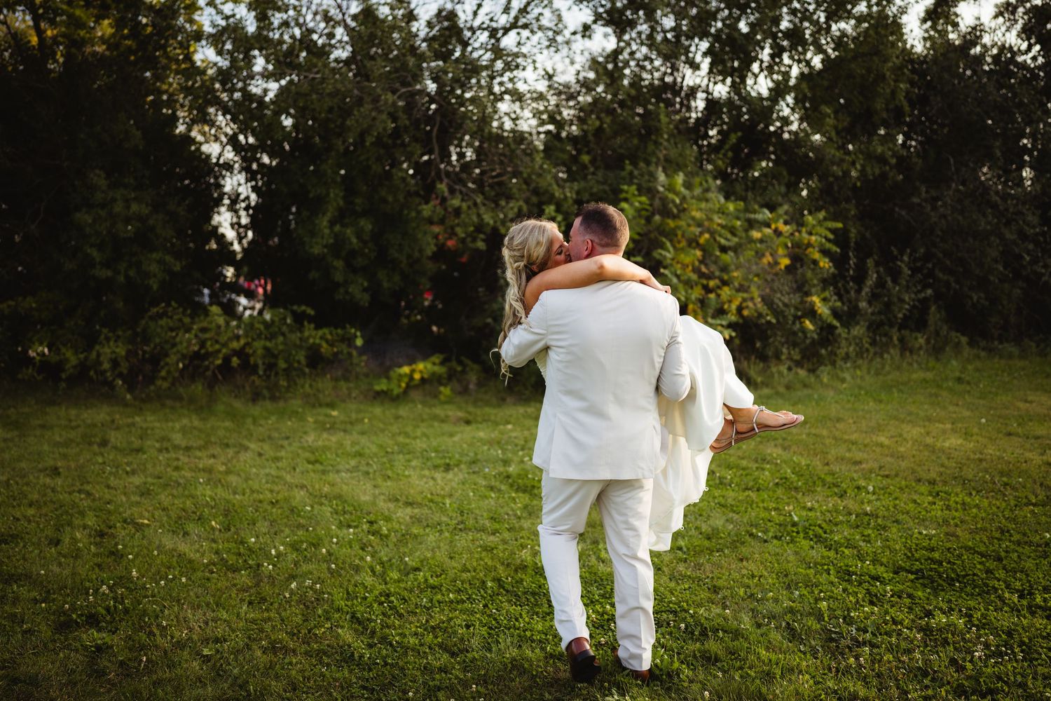 Couple in white outfits strolls together through a lush green garden path during golden hour.