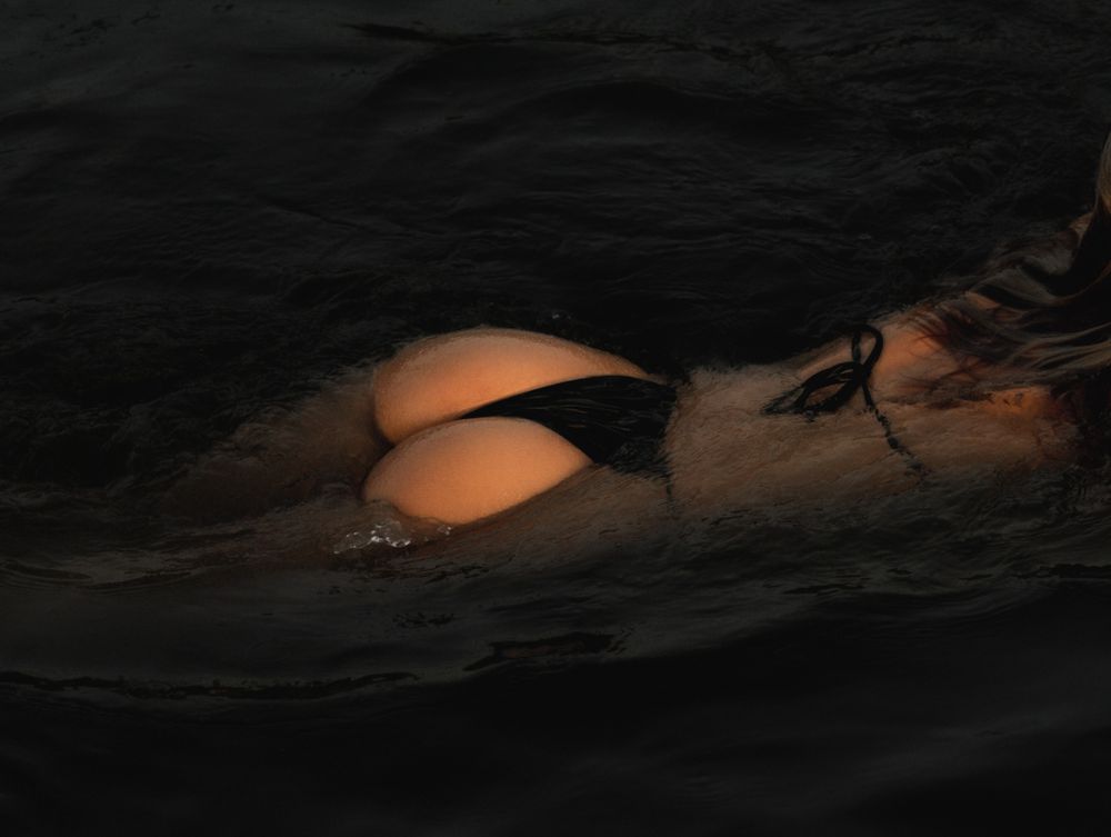 Serene water photography with floating figure creating peaceful dark water reflections.