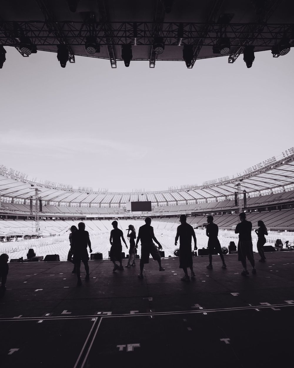 Silhouettes of people walking in a stadium with dramatic black and white lighting creating a moody atmosphere.