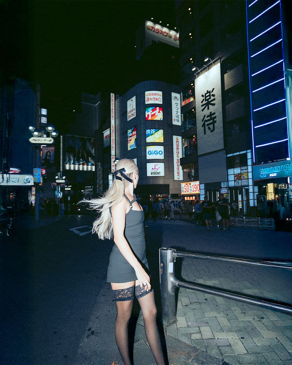 A nighttime urban street scene in Japan with neon lights and signage illuminating the dark cityscape.