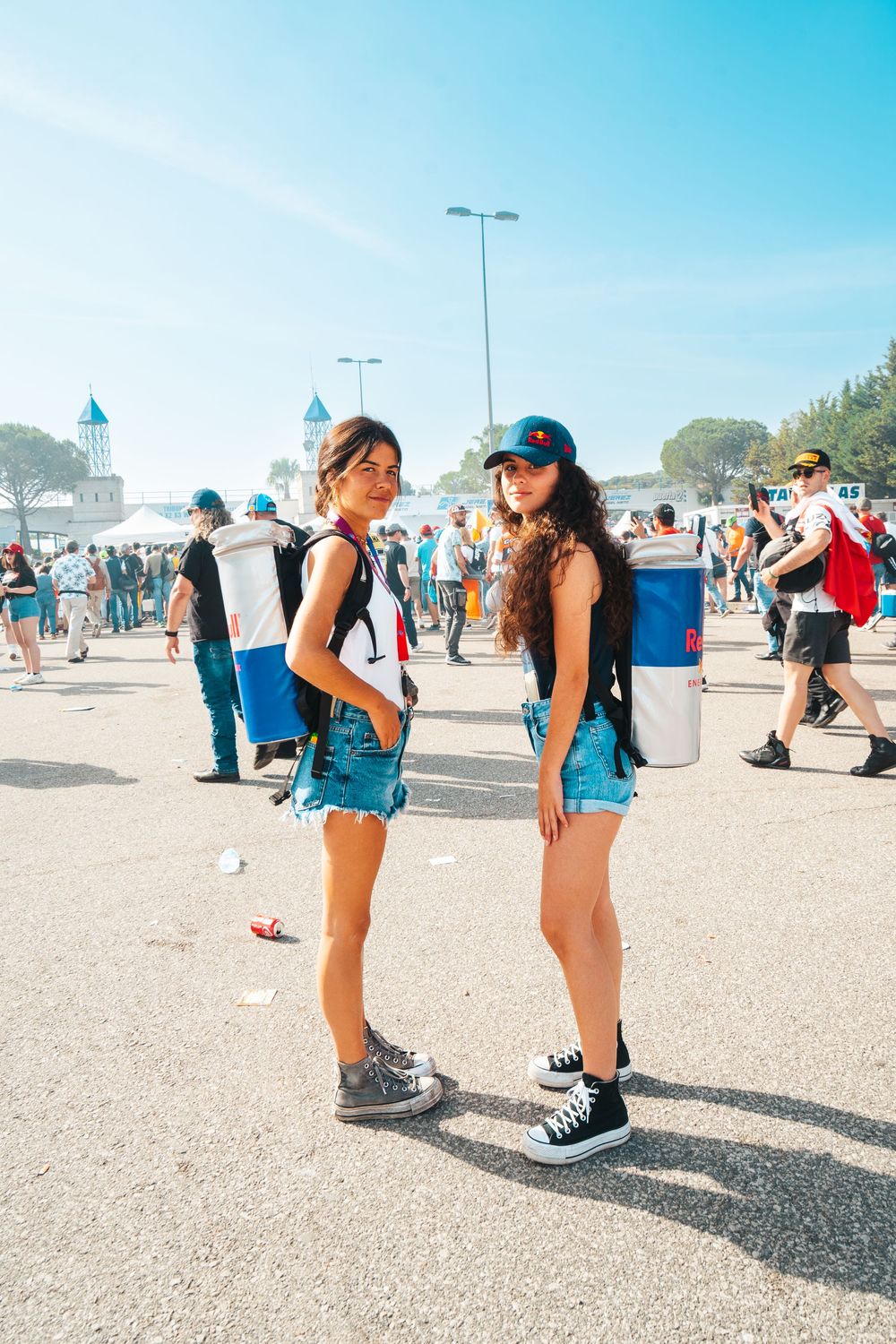 Two people bend down to tie their shoes in a dusty outdoor area with other attendees visible in the background.