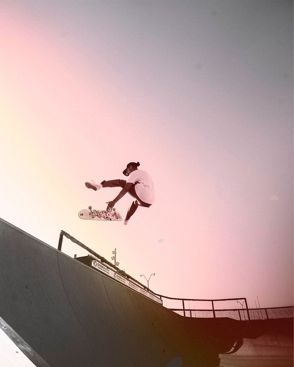 A skateboarder performs a dramatic aerial trick against a pink sunset sky silhouetted on a halfpipe ramp.