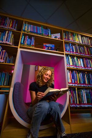 Student reading book in modern curved library nook with pink accent wall.