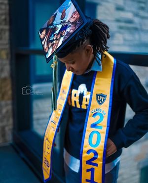 Graduate wearing decorated cap and class of 2021 sash looking down thoughtfully.