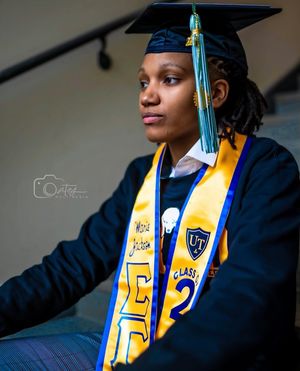 Graduate in academic regalia with blue and gold honor cords posing for portrait.