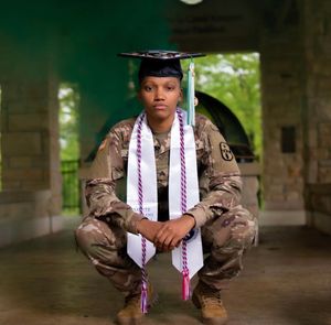 Military graduate in camouflage uniform poses with graduation stole and cap.