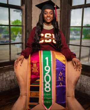 Graduate in maroon sweatshirt displaying multiple honor cords and stoles in formal portrait.