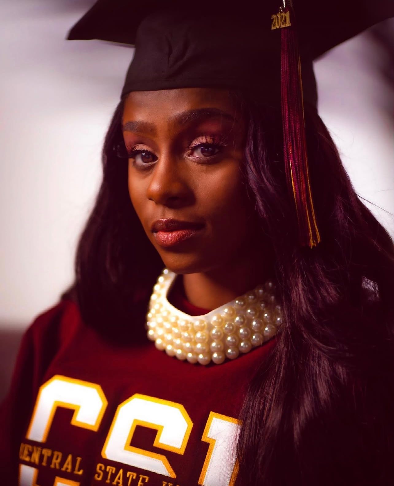 Graduation portraits featuring maroon jersey and pearl necklace against dark background.