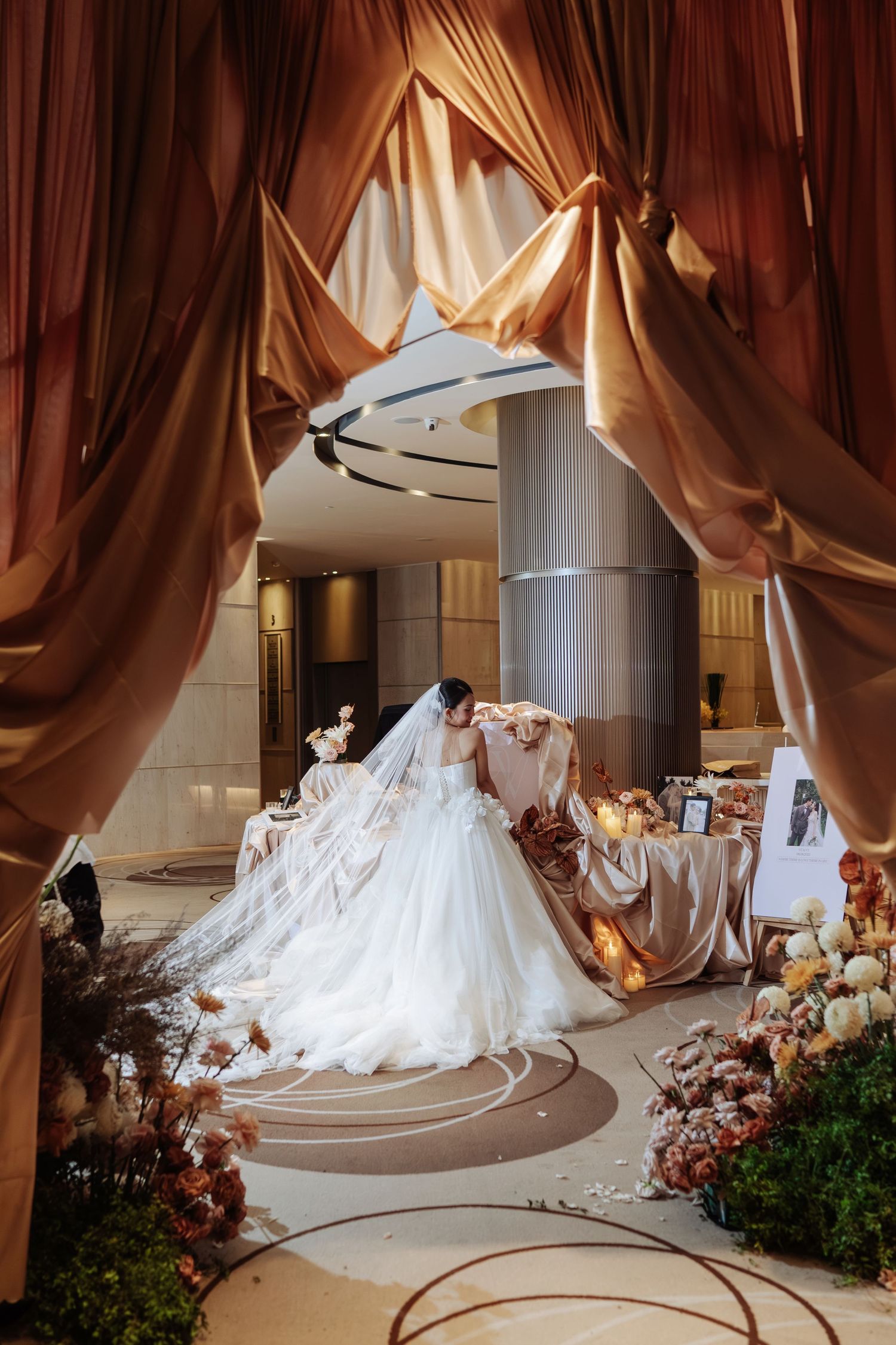 Bride in white ballgown with long veil walking through dramatic golden draped wedding venue.