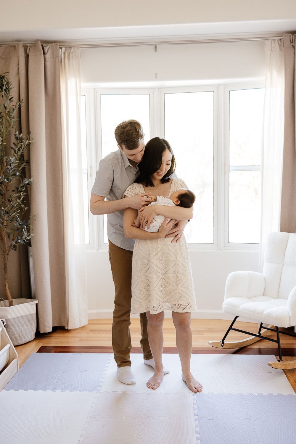 A mother and father cuddle their newborn baby in front of their beautiful bay window in the Bay Area of California