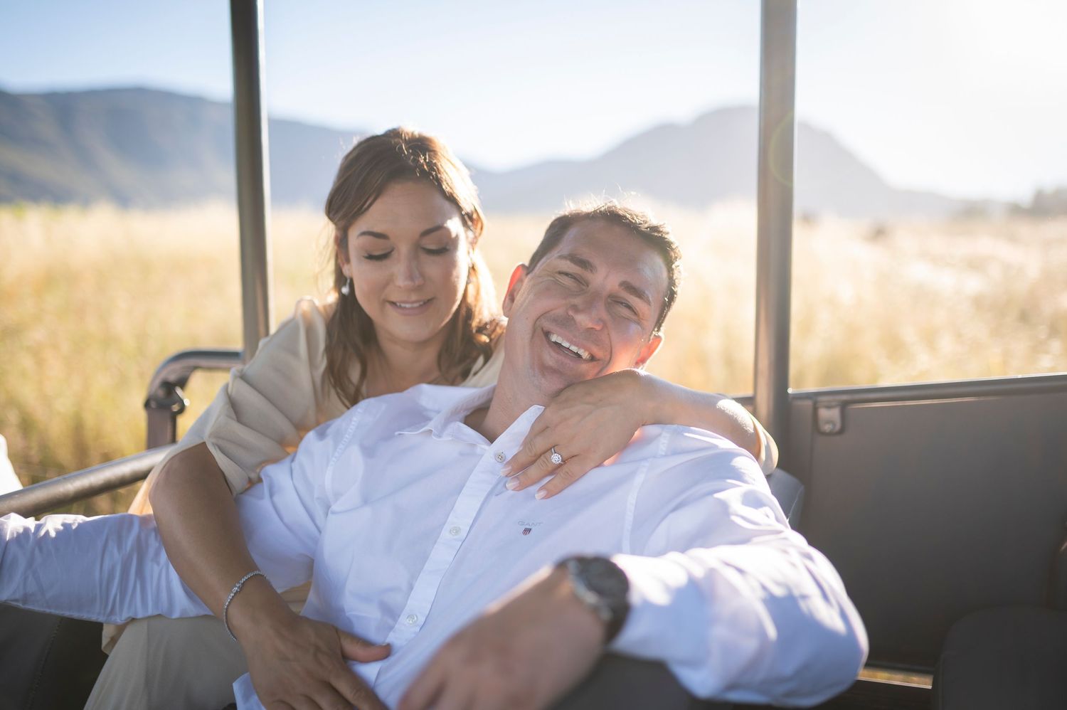Couple sharing a joyful moment while relaxing in a vehicle with scenic mountain landscape in the background.