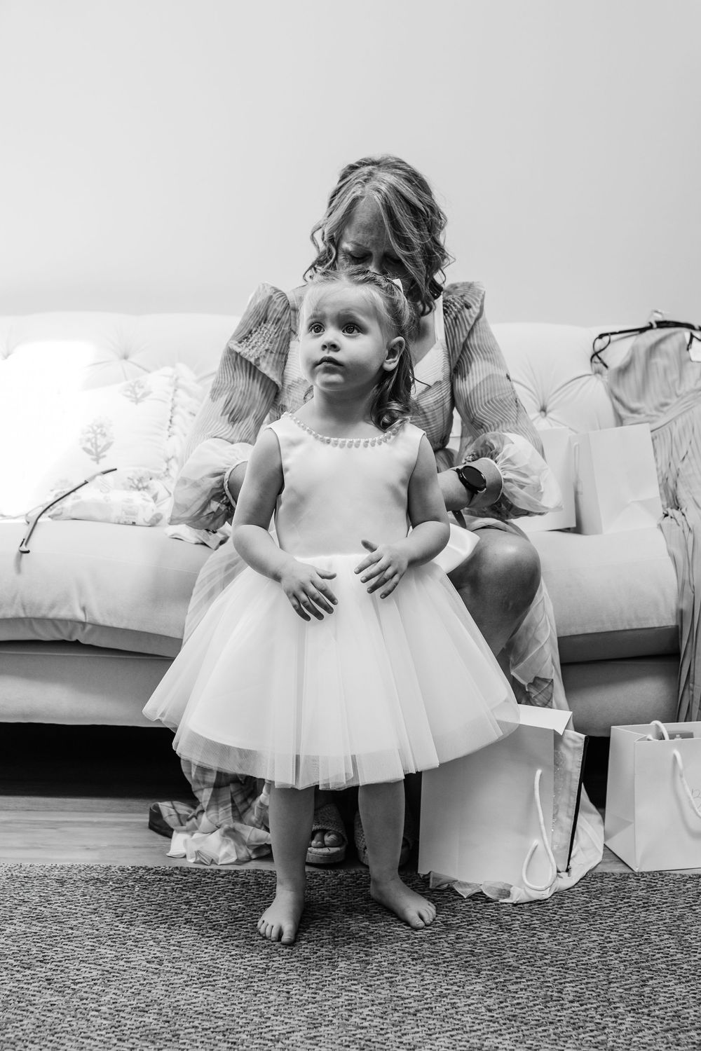 Young attendant in a white tulle dress sits on a carpeted floor during a wedding celebration.
