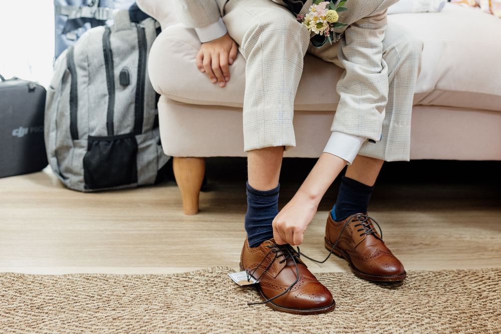 Close-up of polished brown leather dress shoes worn with light colored pants on hardwood floor.