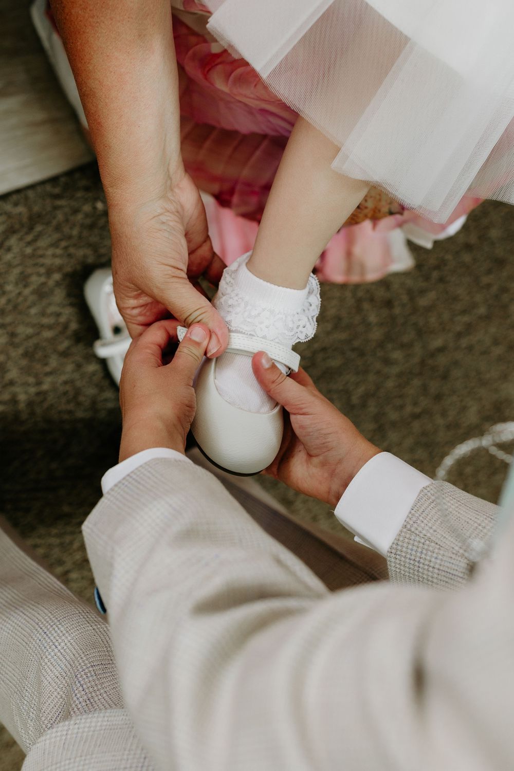Hands adjusting a delicate white lace anklet or sock on someone wearing formal attire.