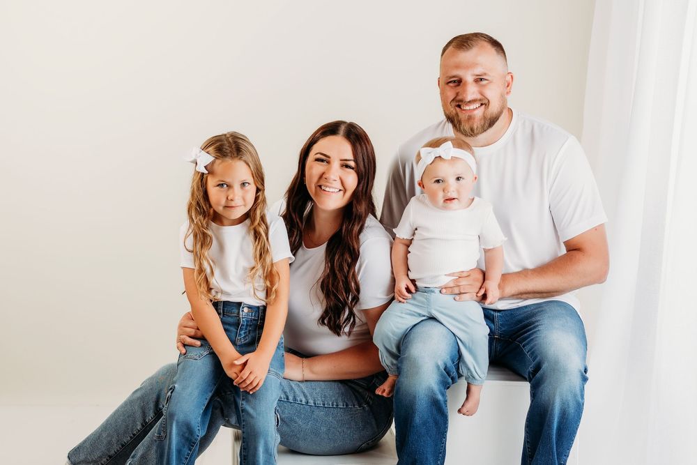 Family sitting together wearing matching white and denim outfits in bright studio setting.
