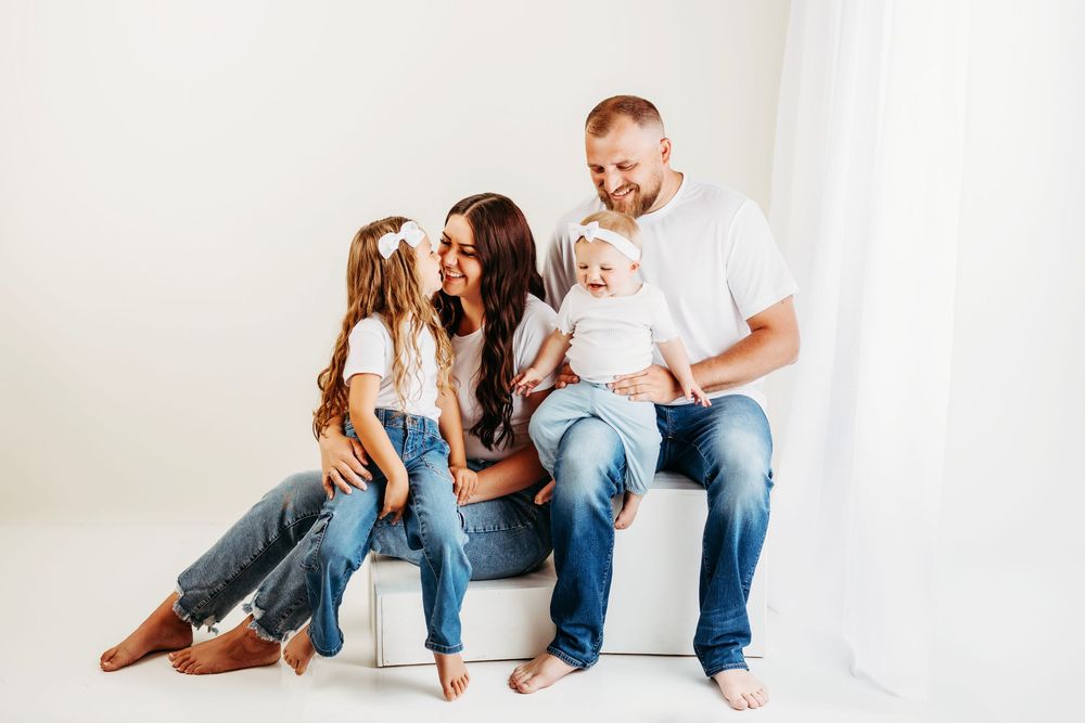 Family in white attire lounges together in casual poses on a white background.