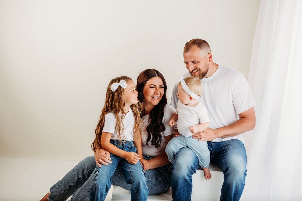 Parents sitting on floor playing with small child in white bright room.